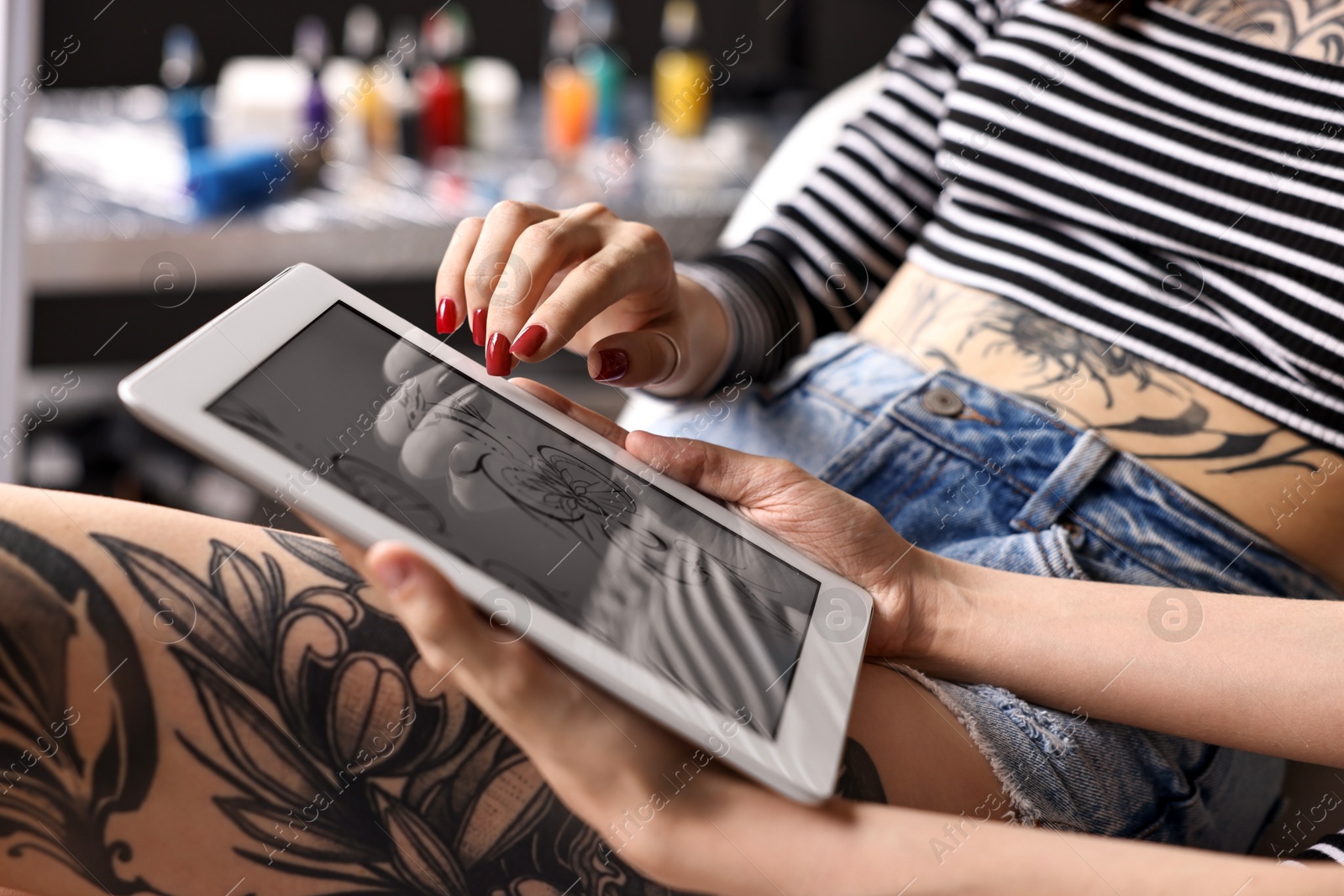 Photo of Tattoo artist showing tablet with sketch to client in salon, closeup