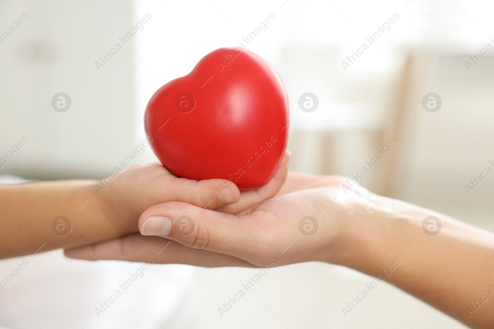 Photo of Little girl and her mother with red heart figure indoors, closeup