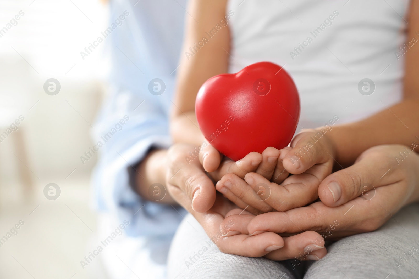 Photo of Little girl and her mother with red heart figure indoors, closeup