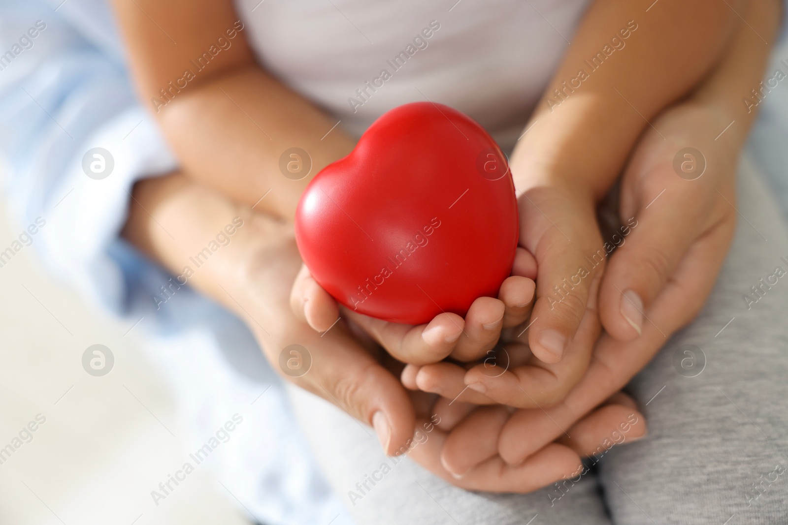 Photo of Little girl and her mother with red heart figure indoors, closeup