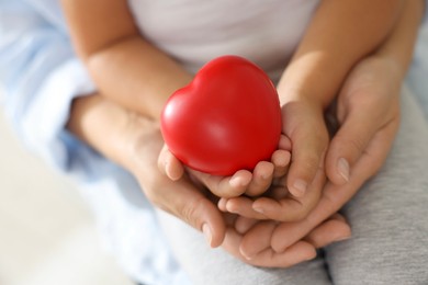 Photo of Little girl and her mother with red heart figure indoors, closeup