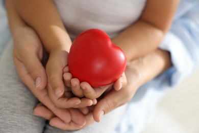 Photo of Little girl and her mother with red heart figure indoors, closeup