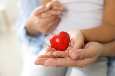 Photo of Little girl and her mother with red heart figure indoors, closeup