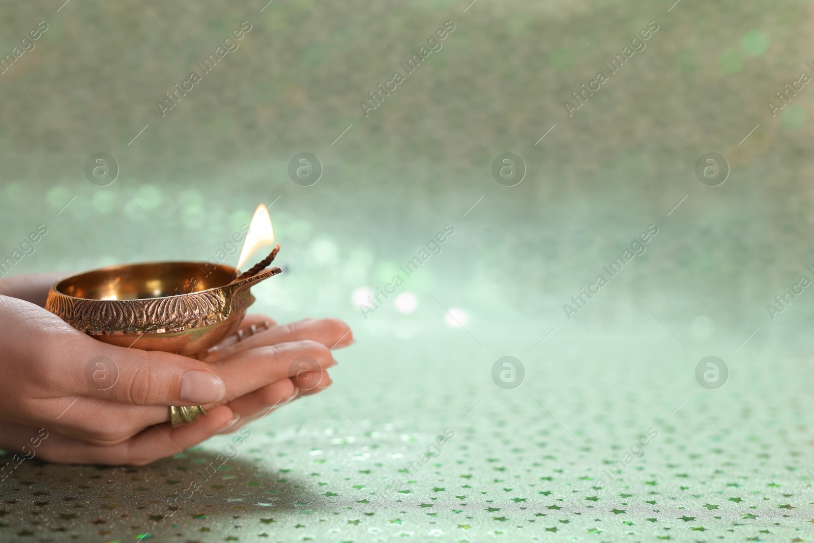 Photo of Diwali celebration. Woman holding lit diya lamp on color background, closeup. Space for text