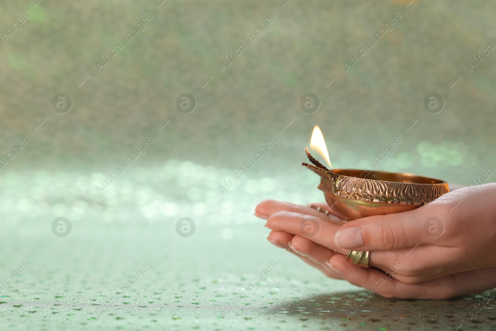 Photo of Diwali celebration. Woman holding lit diya lamp on color background, closeup. Space for text