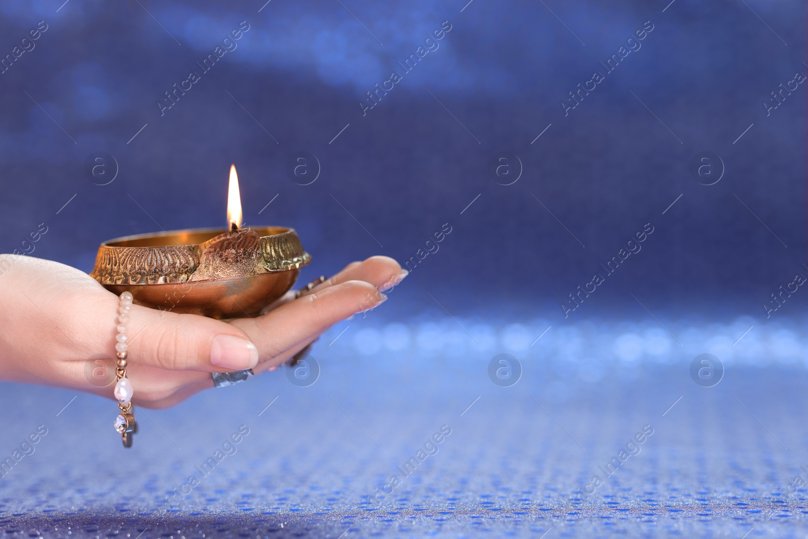 Photo of Diwali celebration. Woman holding lit diya lamp on blue background, closeup. Space for text