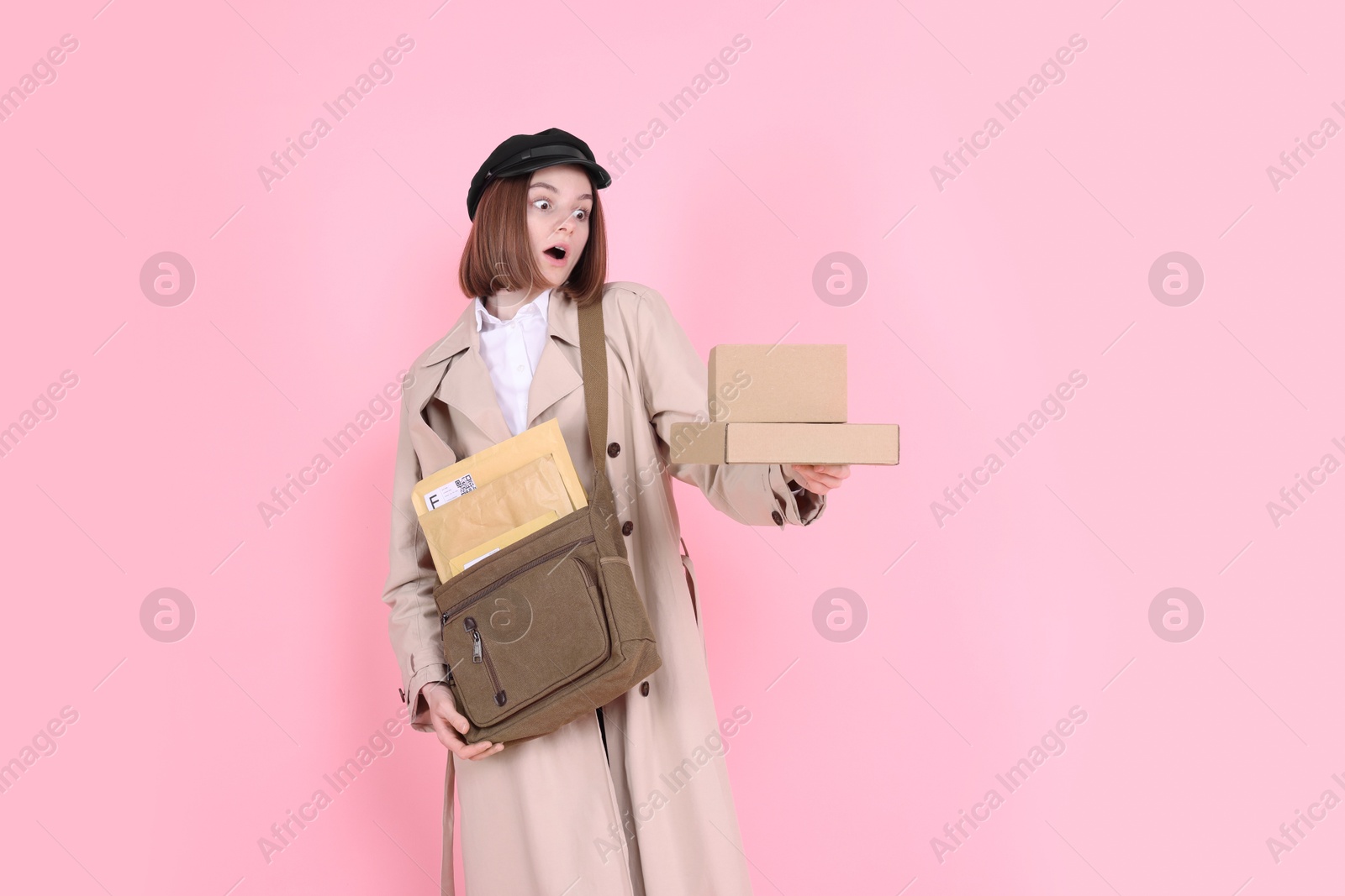 Photo of Emotional postwoman with bag and parcels on pink background. Space for text