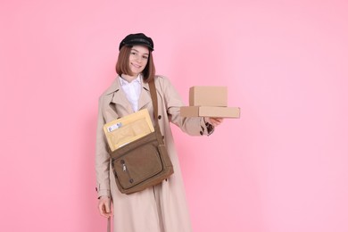 Photo of Happy postwoman with bag and parcels on pink background. Space for text