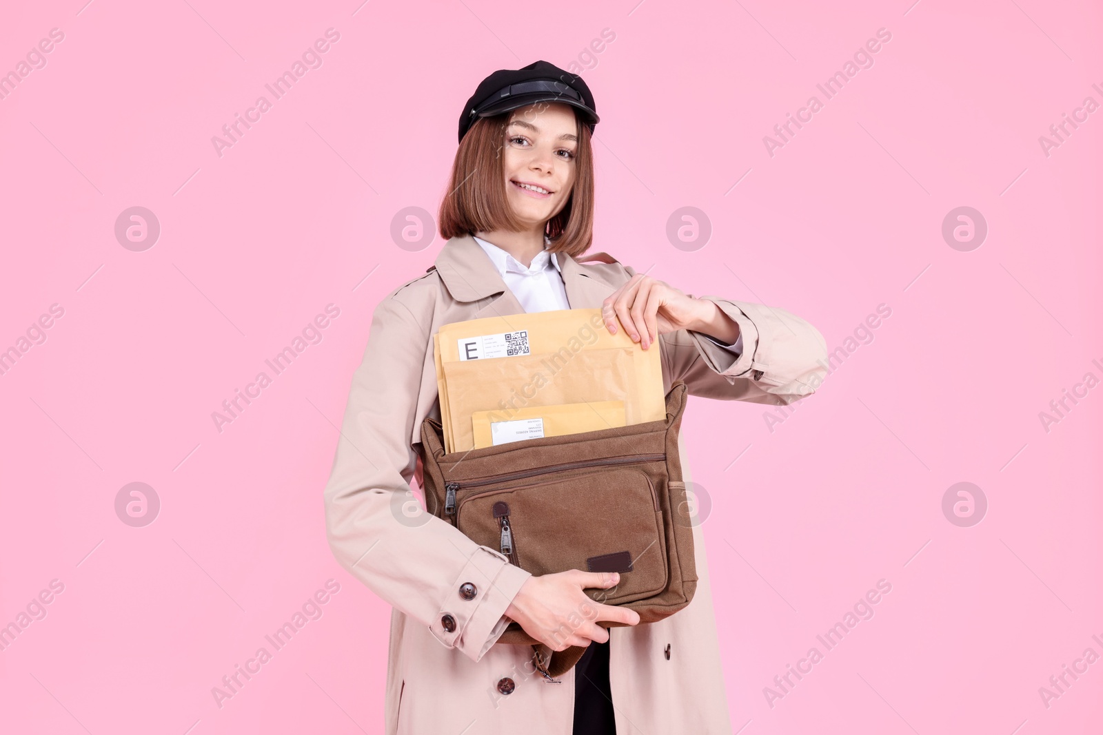 Photo of Happy postwoman with bag and envelopes on pink background