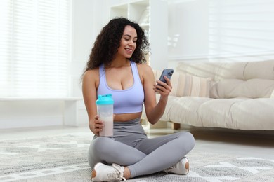 Photo of Beautiful woman with protein shake and smartphone at home