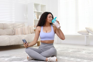 Photo of Beautiful woman with smartphone drinking protein shake at home