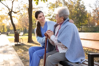 Photo of Elderly woman with walking cane and her caregiver in park