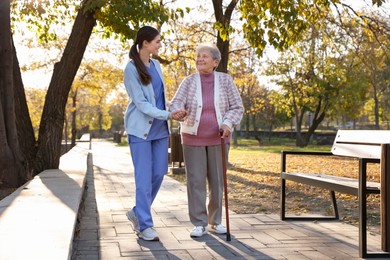 Photo of Elderly woman with walking cane and her caregiver in park