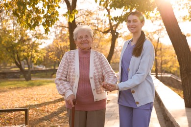 Photo of Elderly woman with walking cane and her caregiver in park