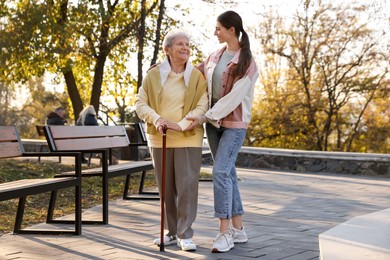 Photo of Elderly woman with walking cane and her caregiver in park