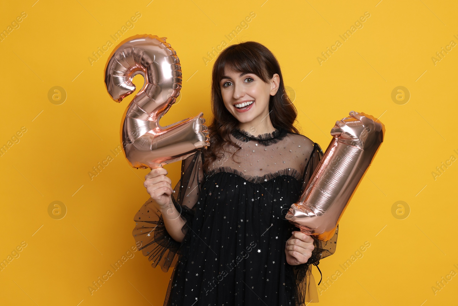 Photo of Coming of age party - 21st birthday. Young woman holding number shaped balloons on yellow background