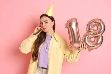 Photo of Coming of age party - 18th birthday. Happy young woman with number shaped balloons, hat and blower on pink background