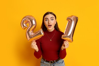 Photo of Coming of age party - 21st birthday. Emotional young woman with number shaped balloons on yellow background