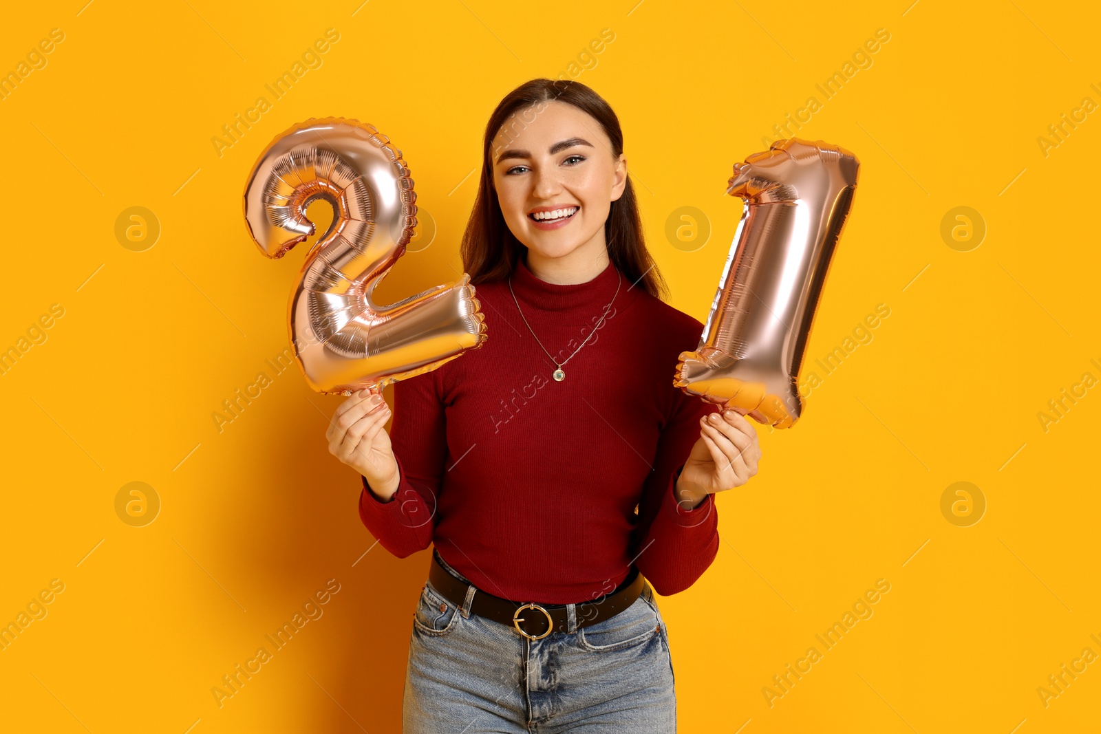 Photo of Coming of age party - 21st birthday. Happy young woman with number shaped balloons on yellow background, space for text