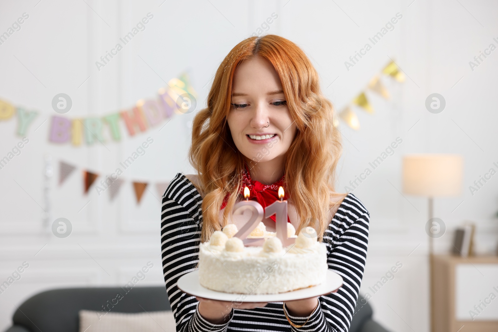 Photo of Coming of age party - 21st birthday. Happy young woman holding tasty cake with number shaped candles at home