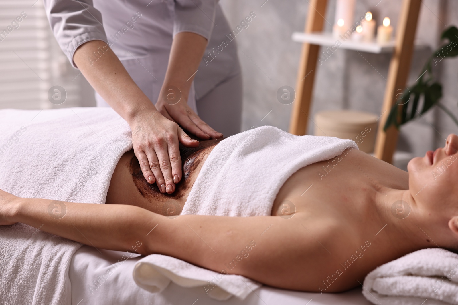 Photo of Woman undergoing chocolate body wrap treatment in spa salon, closeup