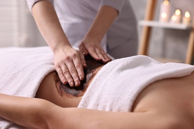 Photo of Woman undergoing chocolate body wrap treatment in spa salon, closeup