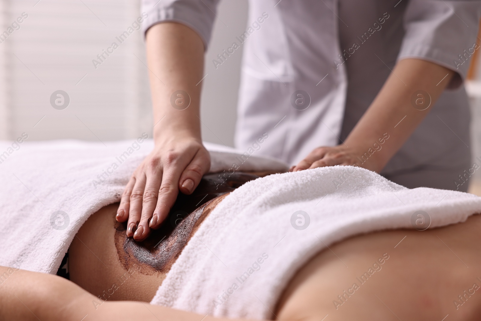 Photo of Woman undergoing chocolate body wrap treatment in spa salon, closeup