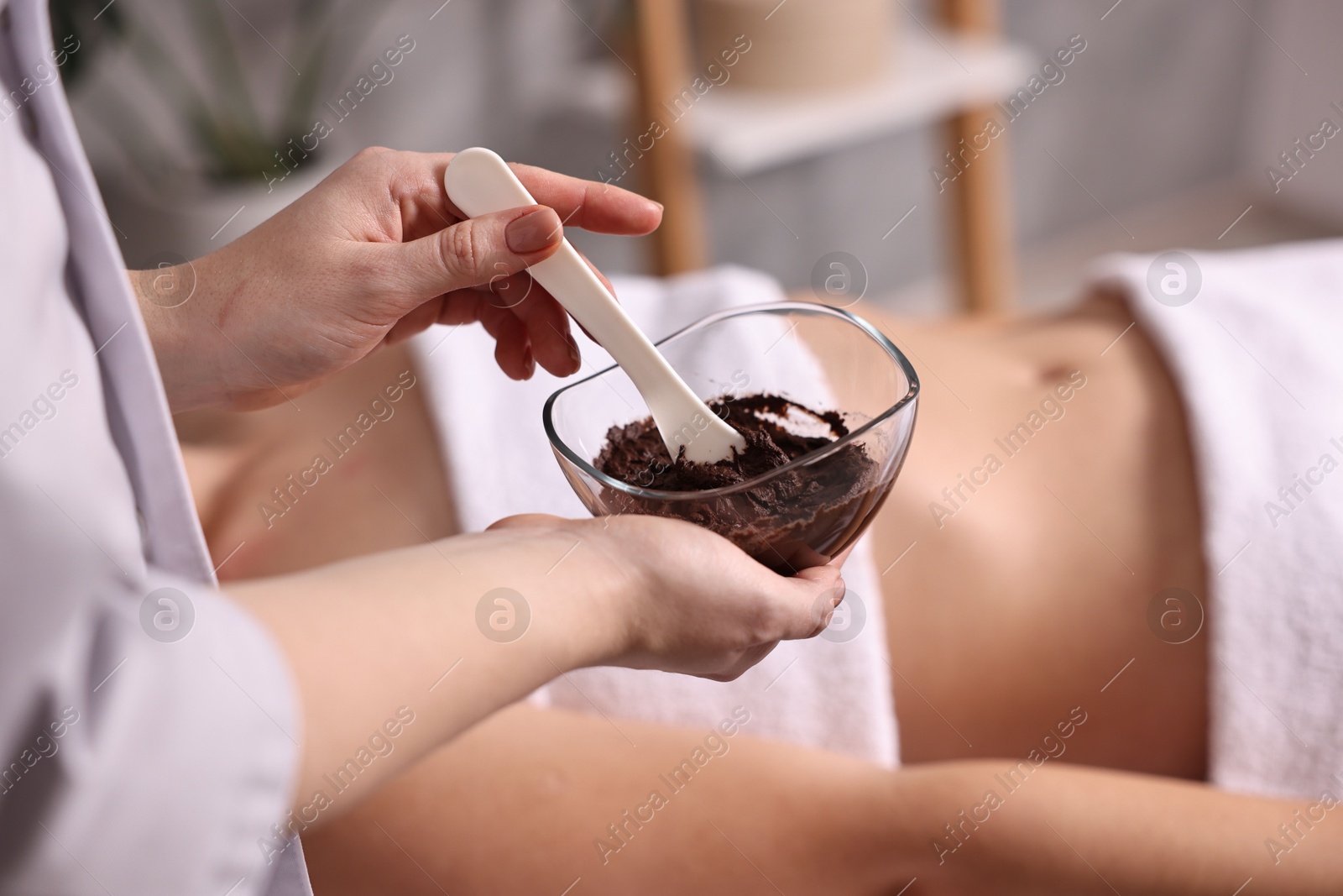 Photo of Spa worker with cosmetic product for chocolate body wrap near woman in salon, closeup