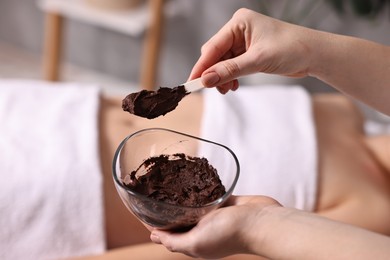 Photo of Spa worker with cosmetic product for chocolate body wrap near woman in salon, closeup