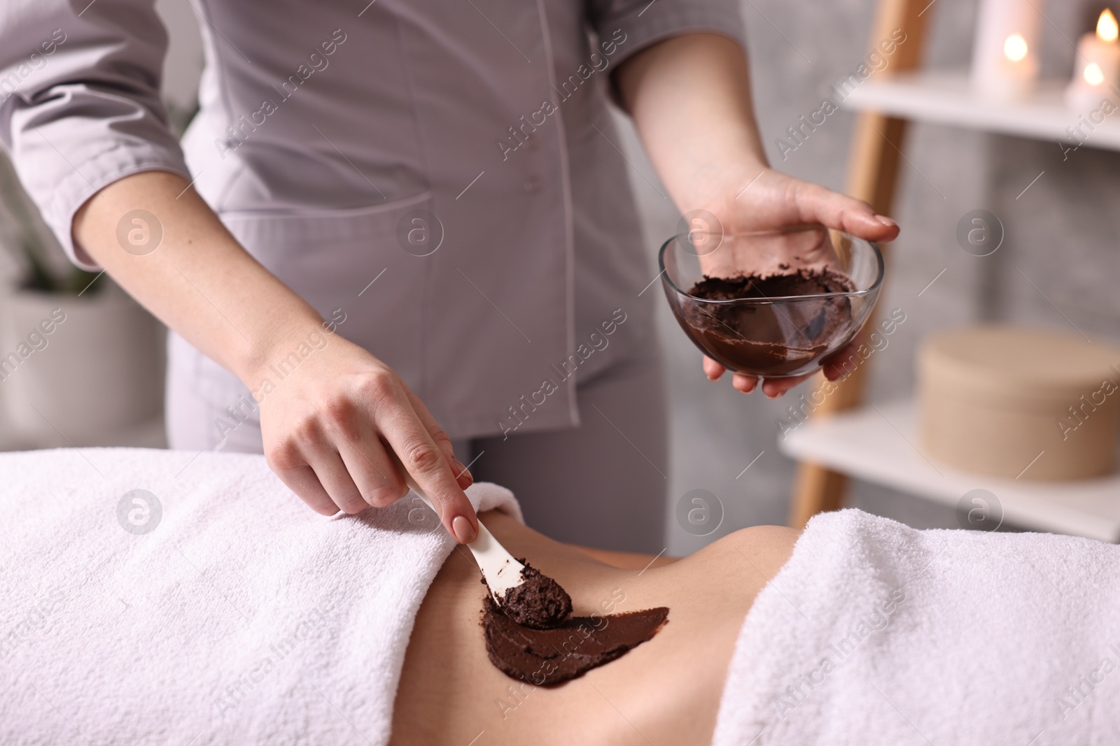 Photo of Chocolate body wrap. Spa worker applying mask onto woman's belly in salon, closeup