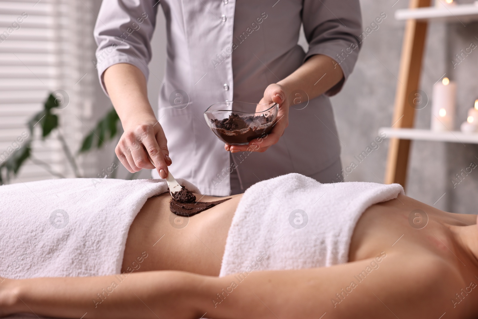 Photo of Chocolate body wrap. Spa worker applying mask onto woman's belly in salon, closeup