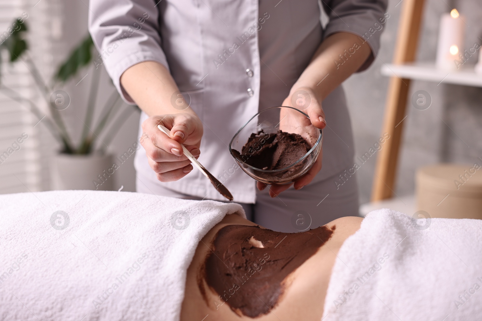 Photo of Chocolate body wrap. Spa worker applying mask onto woman's belly in salon, closeup