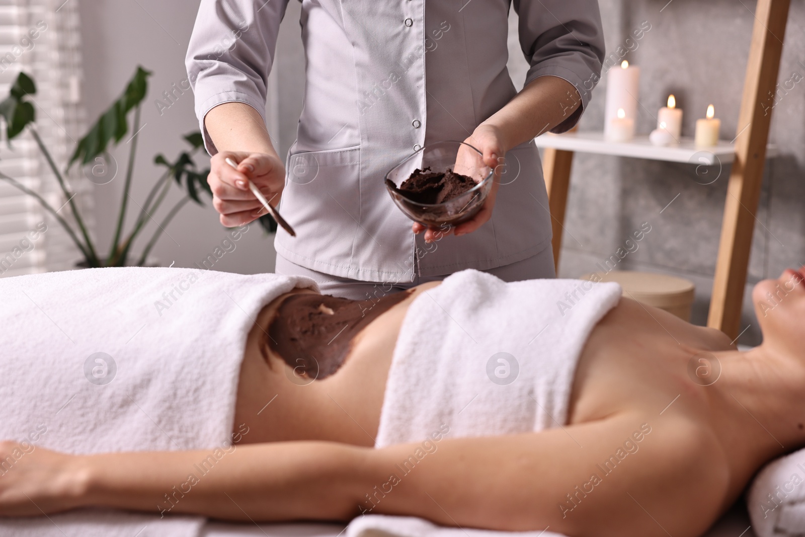 Photo of Chocolate body wrap. Spa worker applying mask onto woman's belly in salon, closeup