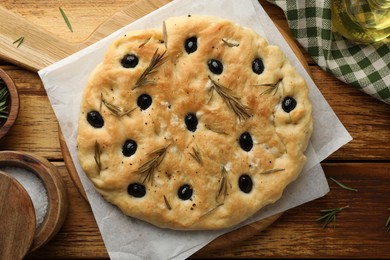 Photo of Delicious focaccia bread with olives, rosemary and salt on wooden table, flat lay