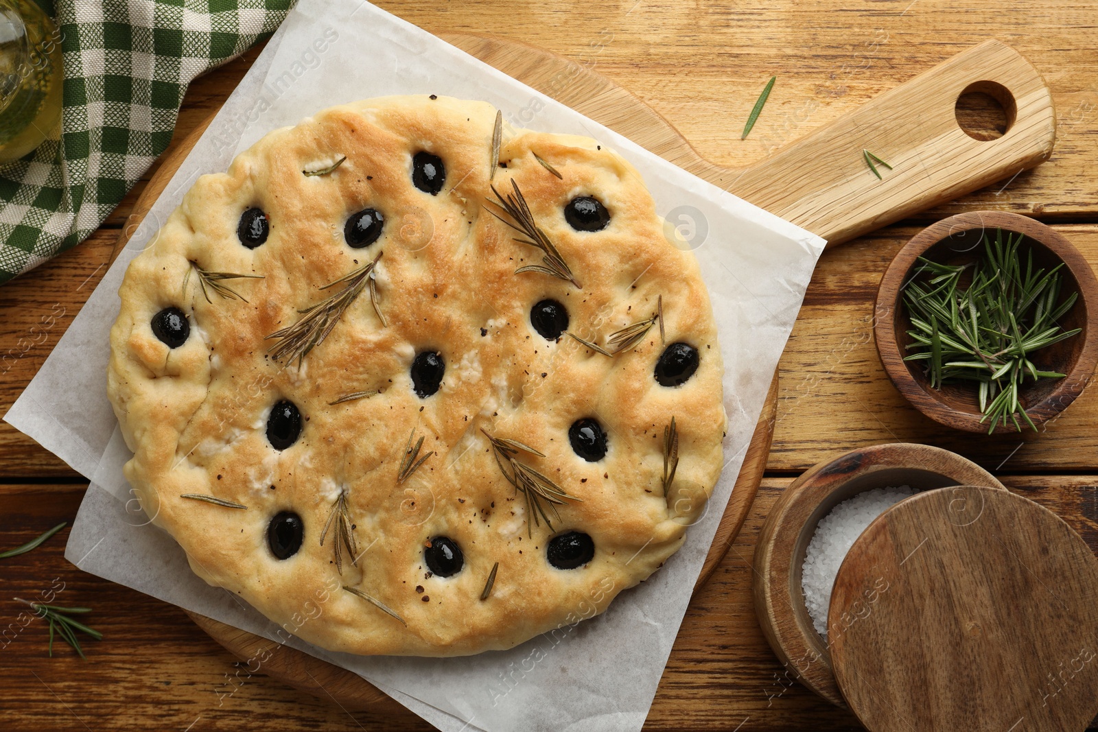 Photo of Delicious focaccia bread with olives, rosemary and salt on wooden table, flat lay