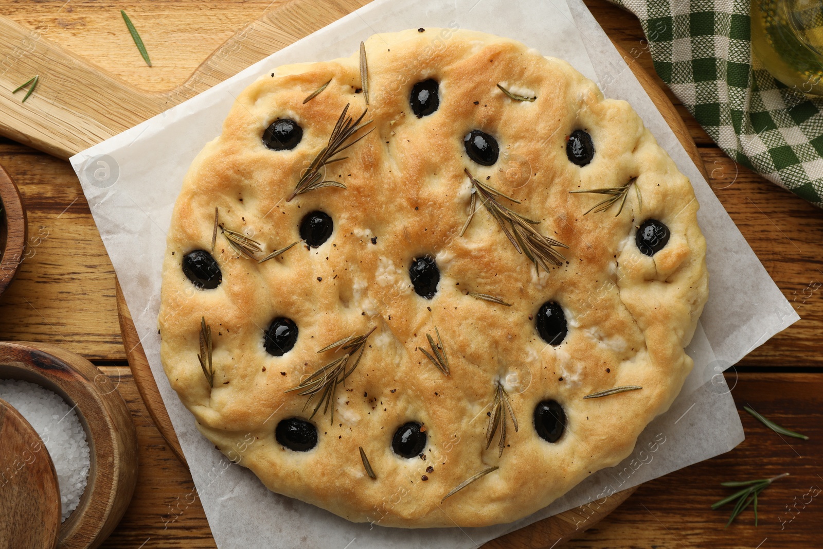 Photo of Delicious focaccia bread with olives, rosemary and salt on wooden table, flat lay