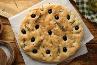 Photo of Delicious focaccia bread with olives, rosemary and salt on wooden table, flat lay