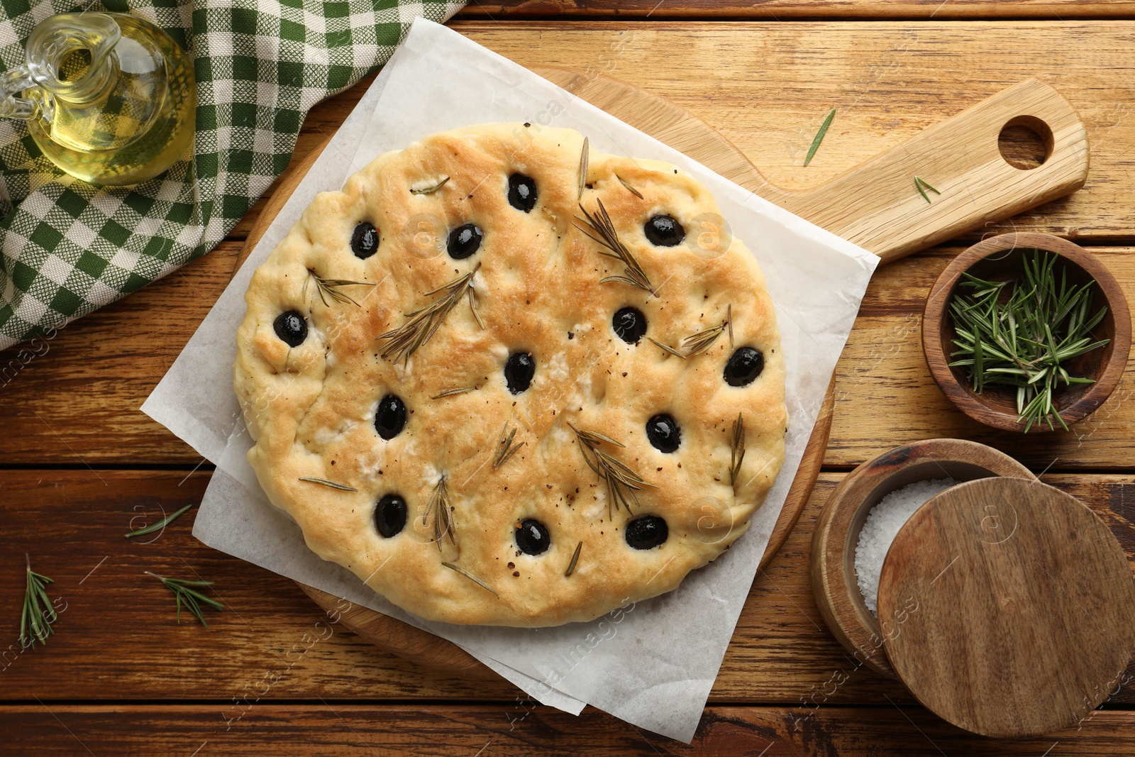 Photo of Delicious focaccia bread with olives, rosemary and salt on wooden table, flat lay