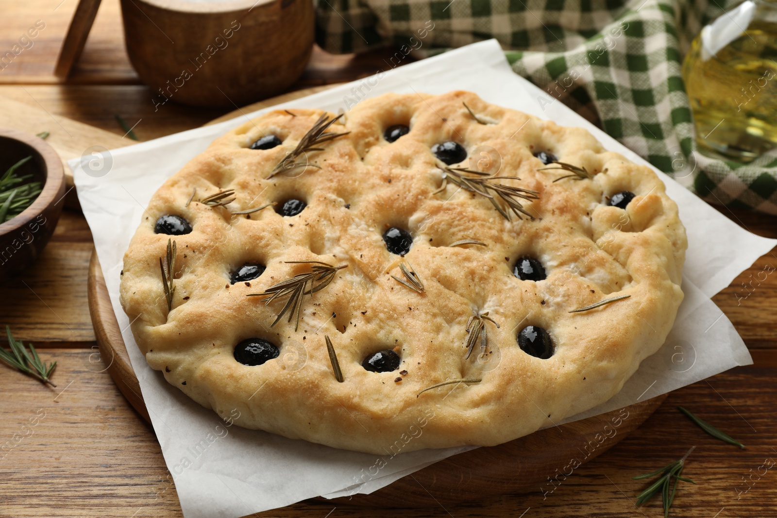 Photo of Delicious focaccia bread with olives and rosemary on wooden table, closeup