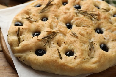 Photo of Delicious focaccia bread with olives and rosemary on wooden table, closeup