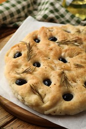 Photo of Delicious focaccia bread with olives and rosemary on wooden table, closeup