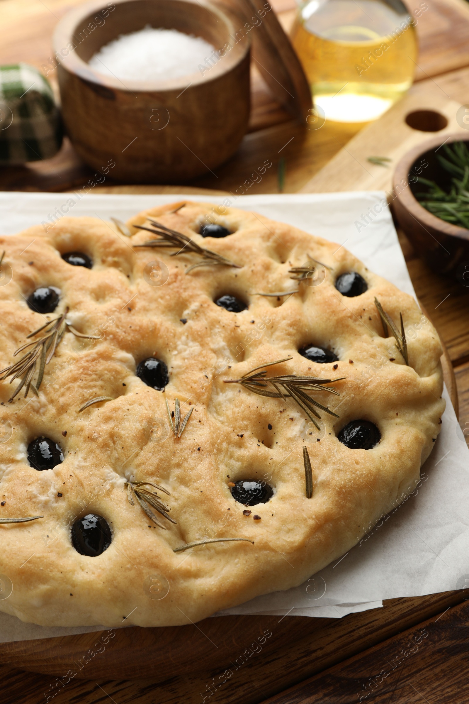 Photo of Delicious focaccia bread with olives, rosemary and salt on wooden table, closeup