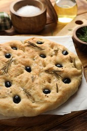 Photo of Delicious focaccia bread with olives, rosemary and salt on wooden table, closeup