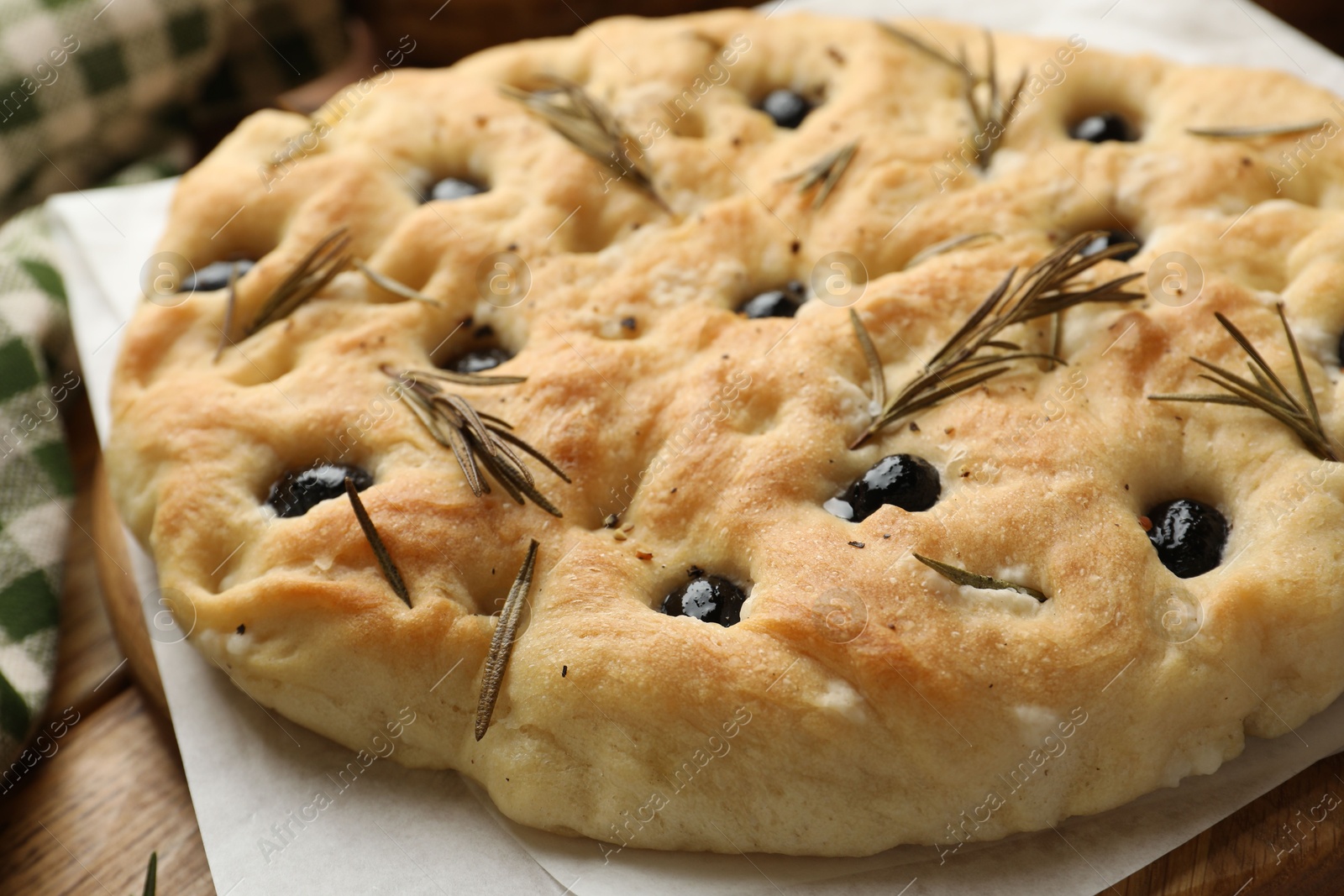 Photo of Delicious focaccia bread with olives and rosemary on table, closeup