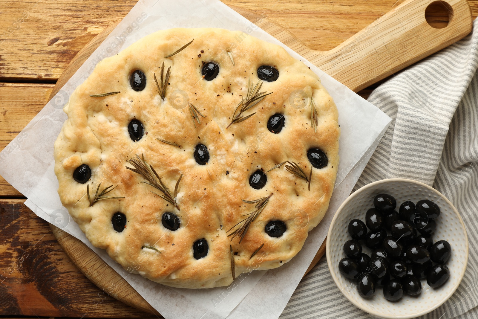 Photo of Delicious focaccia bread with olives and rosemary on wooden table, flat lay