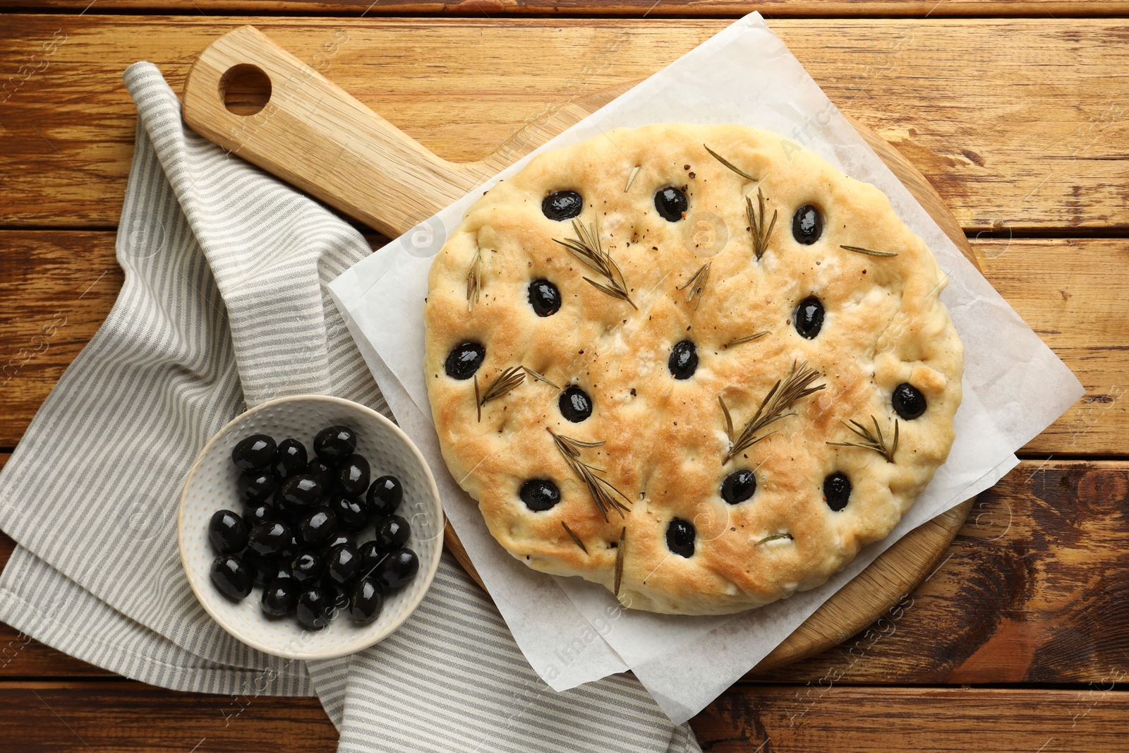 Photo of Delicious focaccia bread with olives and rosemary on wooden table, flat lay