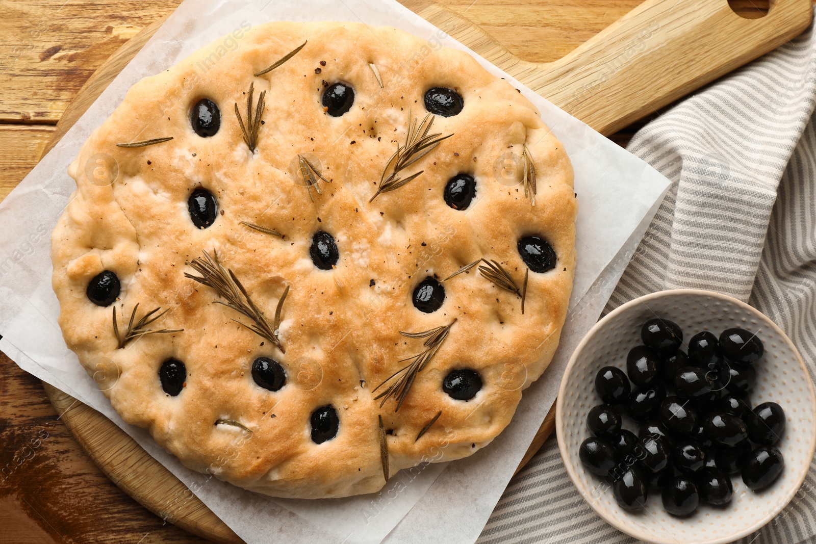 Photo of Delicious focaccia bread with olives and rosemary on wooden table, flat lay