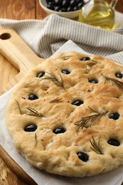 Photo of Delicious focaccia bread with olives and rosemary on table, closeup