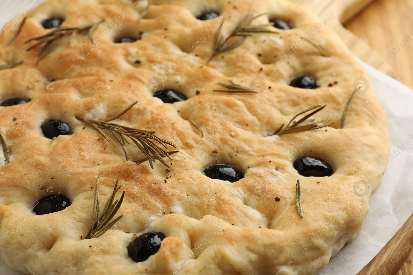 Photo of Delicious focaccia bread with olives and rosemary on table, closeup