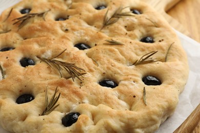 Photo of Delicious focaccia bread with olives and rosemary on table, closeup